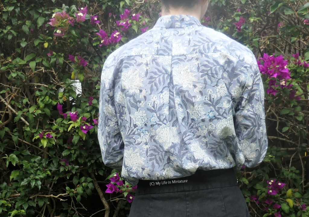 The author stands in front of a hedge, photographed from neck to thighs. She has her back to the camera, so the back of the shirt is visible. A box pleat lines up with the centre seam of the back yoke over the shoulders. The shirt is tucked into the author's black pants.