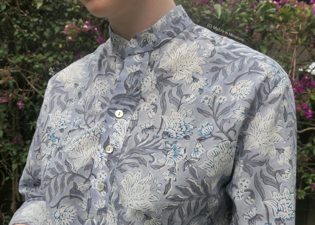 Close-up of the top half of the shirt. The flowers are clearer, and detailing lines in the middle are visible. There are three visible shell buttons on the button placket, and the collarless collar stand sits close to the author's neck.