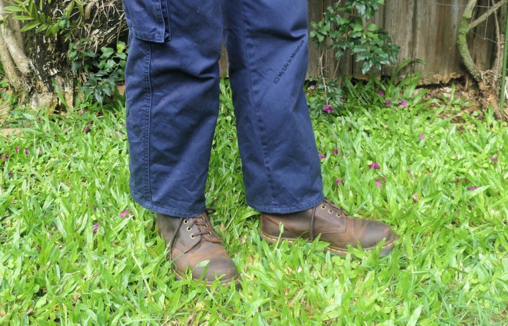 Close-up of the author's lower legs, where she stands on grass against a fence. She's wearing the neatly hemmed navy pants with brown boots.
