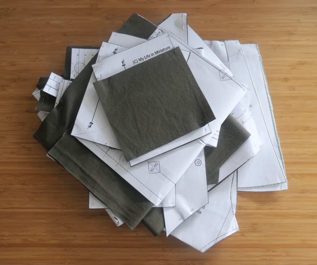 The pant pattern pieces, now cut out, are stacked in a pile on a wood surface. Photographed from above, it's a fairly large pile.