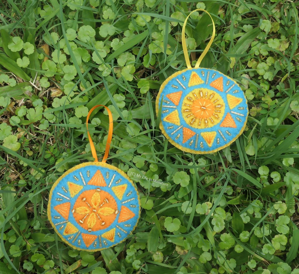 The two sun ornaments are laid on grass, photographed from above. There is not a lot of sunlight, so the beads don't shine as much as they should.
