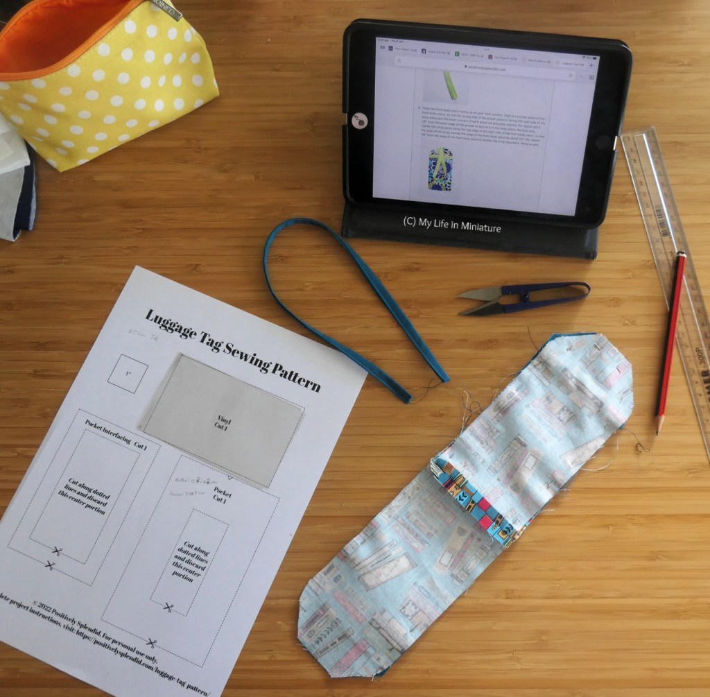 A sewing project in progress, scattered across a wooden surface. Detritus on said surface includes a pattern page, the project itself, a tablet with instructions, thread snips, a pencil, and a ruler.