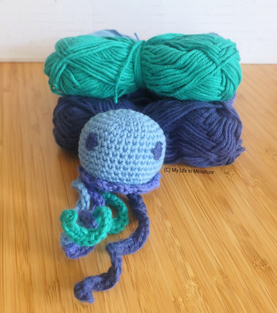 The small jellyfish is photographed leaning against a stack of the four yarns used to make it.