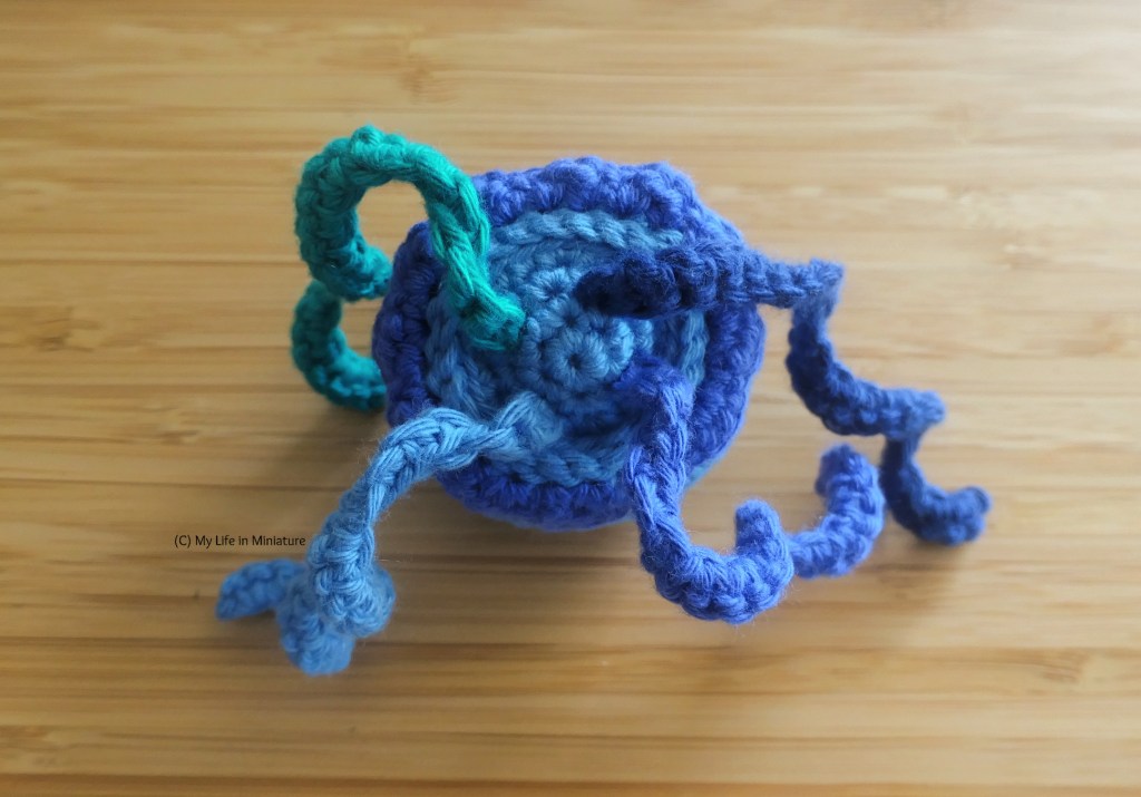 The underside of the smaller jellyfish. Four curly tentacles of different colours have been attached to the base of the body, roughly equidistant.