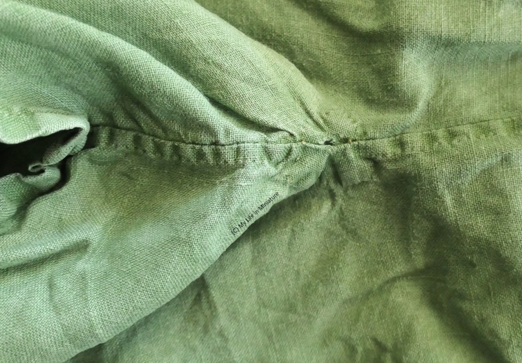 Close-up of the underarm area of one of the author's handmade shirts. Said shirt is green, and has a small hole in the underarm, where the raw edge of the fabric can be seen.