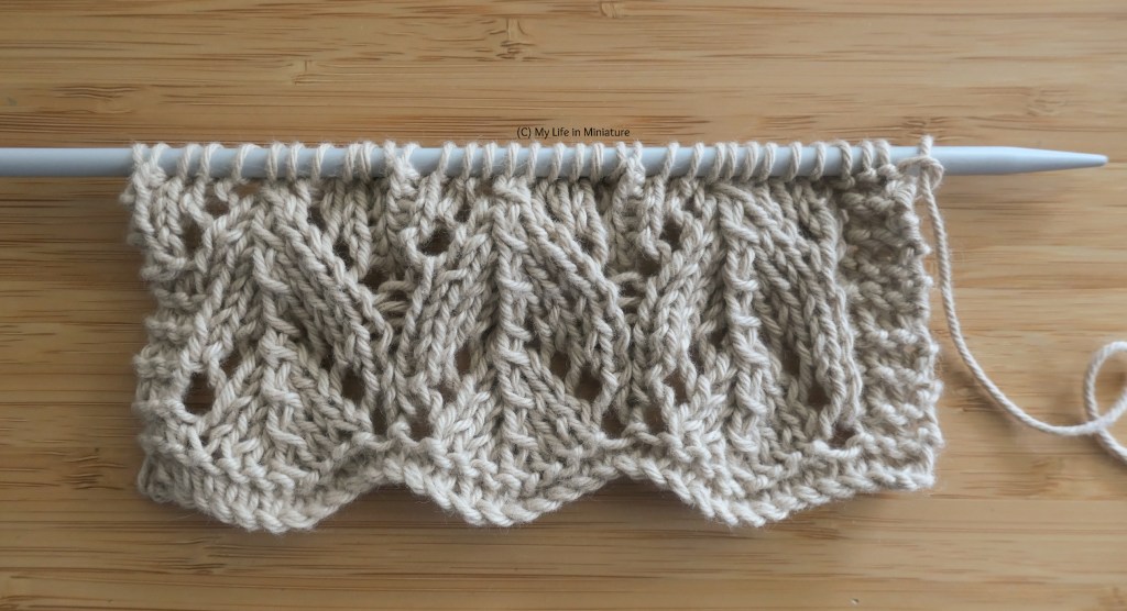 Close-up of the knitted swatch. The lace pattern makes nested triangles, pointing up in parallel columns. The swatch is not very large, in either direction.